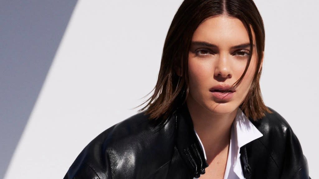 Kendall Jenner wears a white shirt and black leather jacket in MO&Co’s Spring 2025 campaign, set against a white backdrop. 