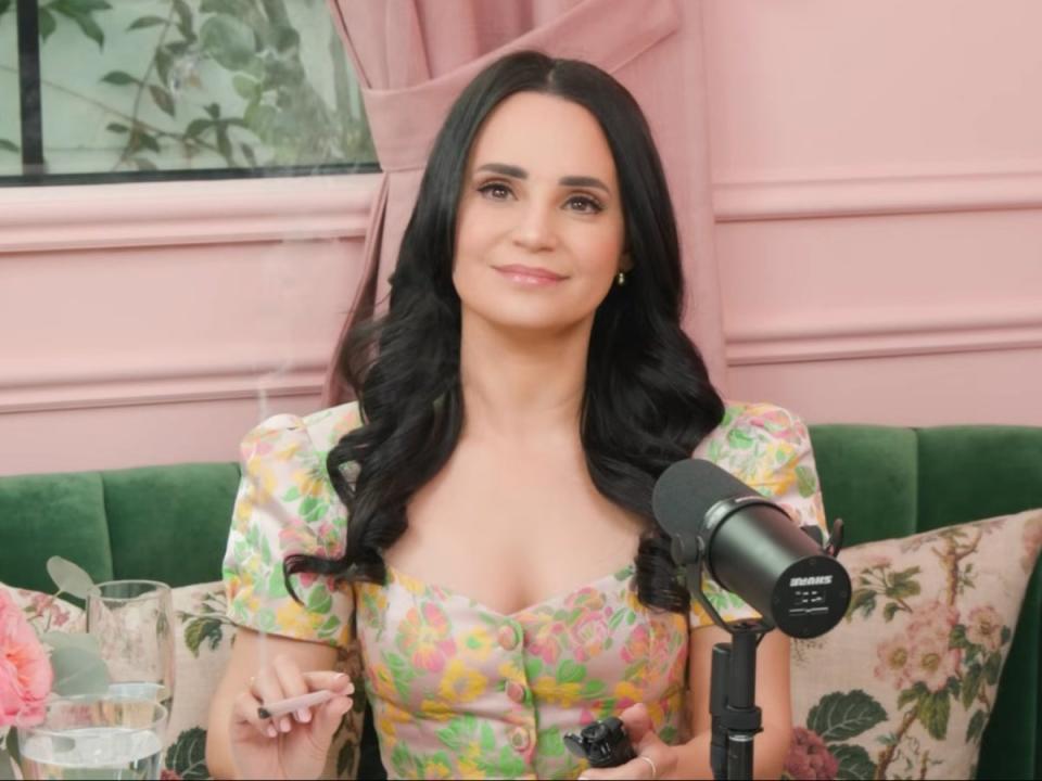 Youtuber Rosanna Pansino holds a joint while sitting on green couch in front of pink wall. She is smoking her dead dads ashes to honor his dying wishes and filming a video for YouTube. 