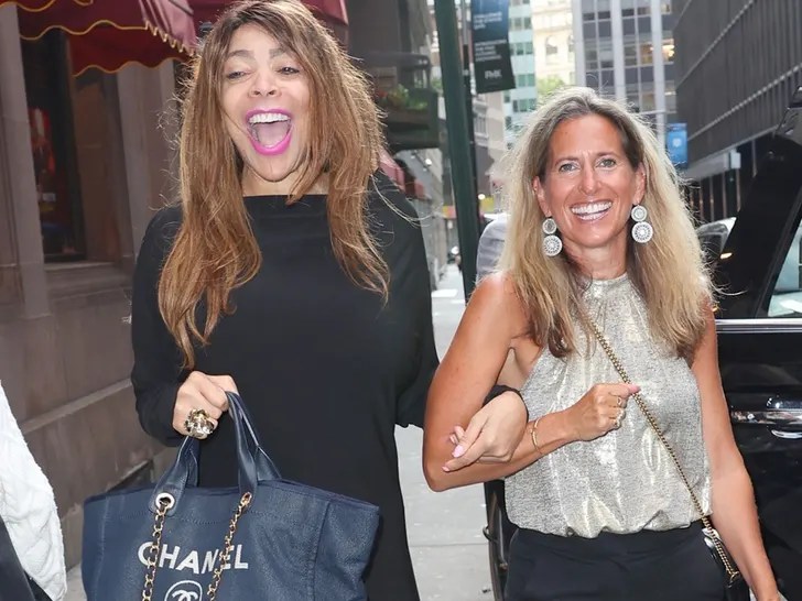 Wendy Williams and her attorney walking in NYC on her 61st birthday to Delmonicos, Wendy is carrying a Chanel purse and smiling with ponk lipstick while holding onto her attorneys arm 