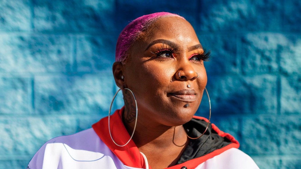 Shirley Raines pink hair smiling while gazing to the side of the screen. 